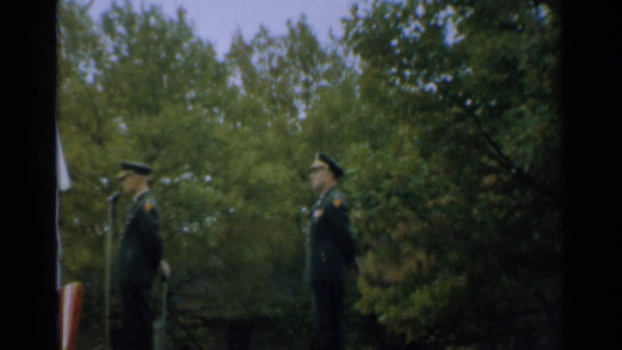 Two uniformed officers stand near microphones outdoors with trees behind them.