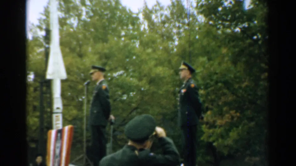 1952 New Hampshire ceremony still with two officers at microphones and a foreground uniformed figure saluting or adjusting a cap.