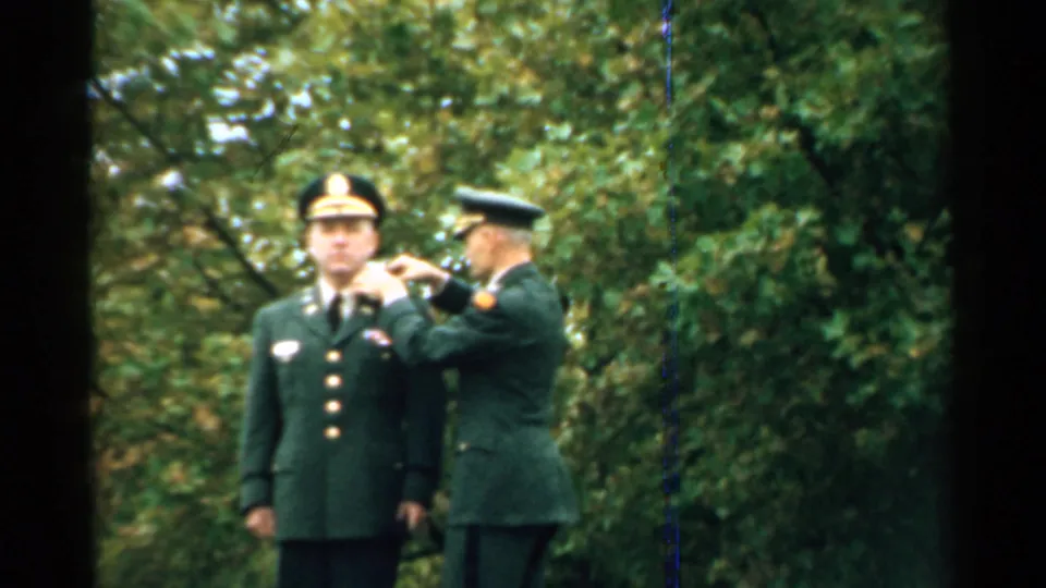 A uniformed officer appears to finish fastening a medal or insignia on a soldier's jacket during the 1952 outdoor ceremony.