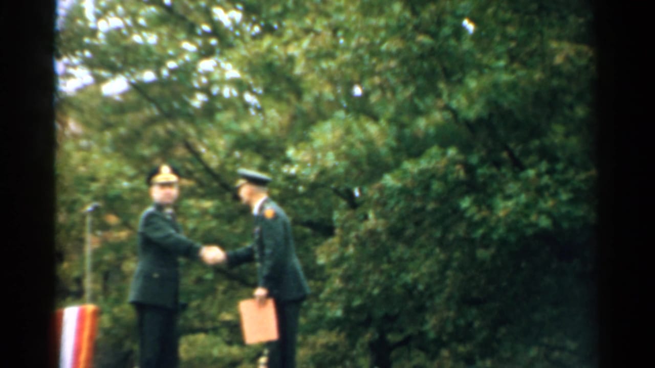 Two uniformed men shake hands after a medal presentation outdoors.