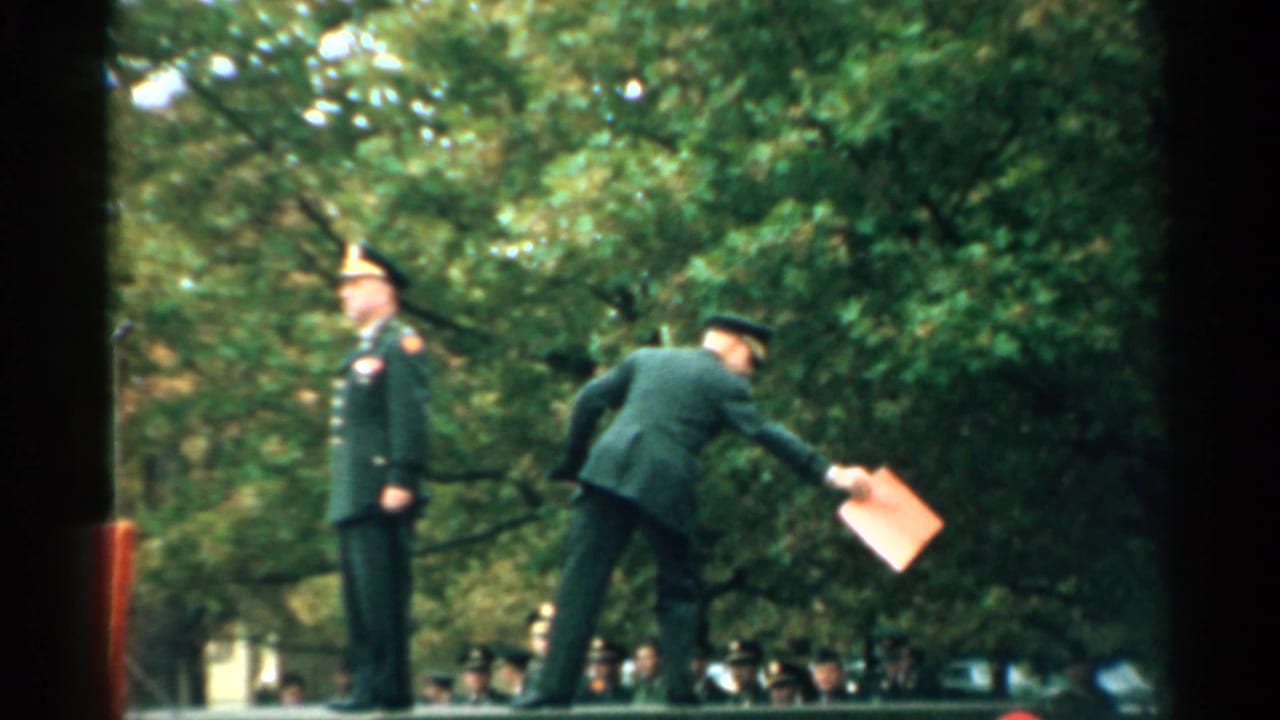 Officer on a raised platform as another uniformed man bends forward holding a folder.
