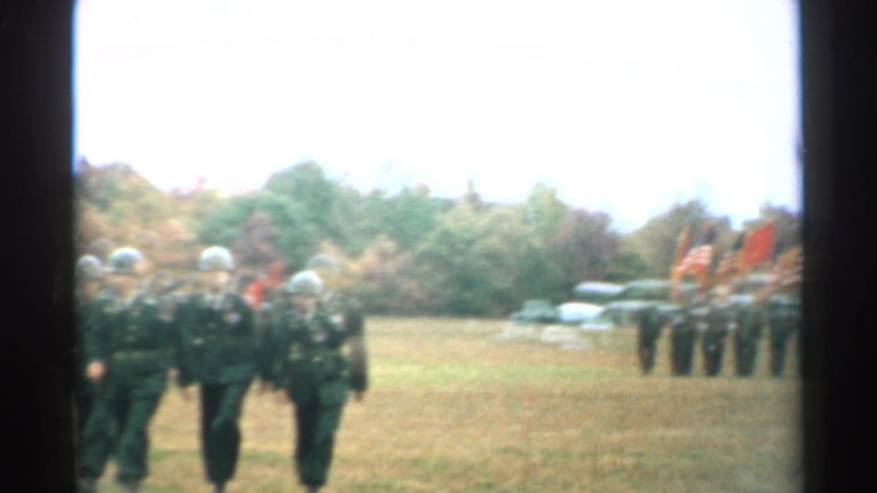 Soldiers in steel helmets stand and move across a grassy New Hampshire field during a 1952 outdoor military ceremony.