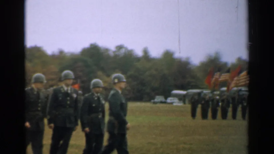 Uniformed soldiers cross a grassy New Hampshire ceremony field in 1952, with flags and another formation visible to the side.
