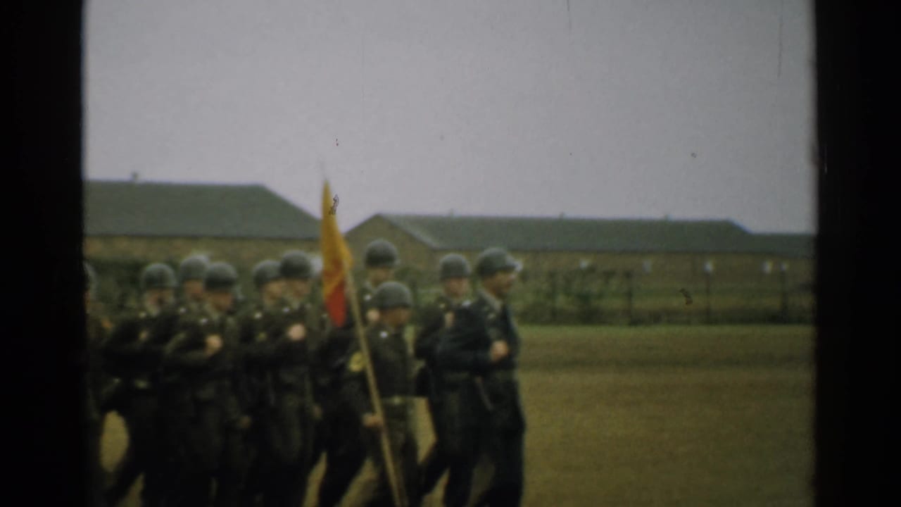 A column of helmeted soldiers marches with a color flag on a base field.