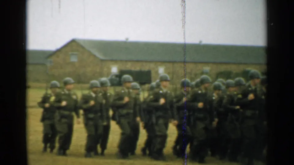 In 1952 New Hampshire home-movie footage, helmeted soldiers in dark uniforms march across a grassy military-base field.