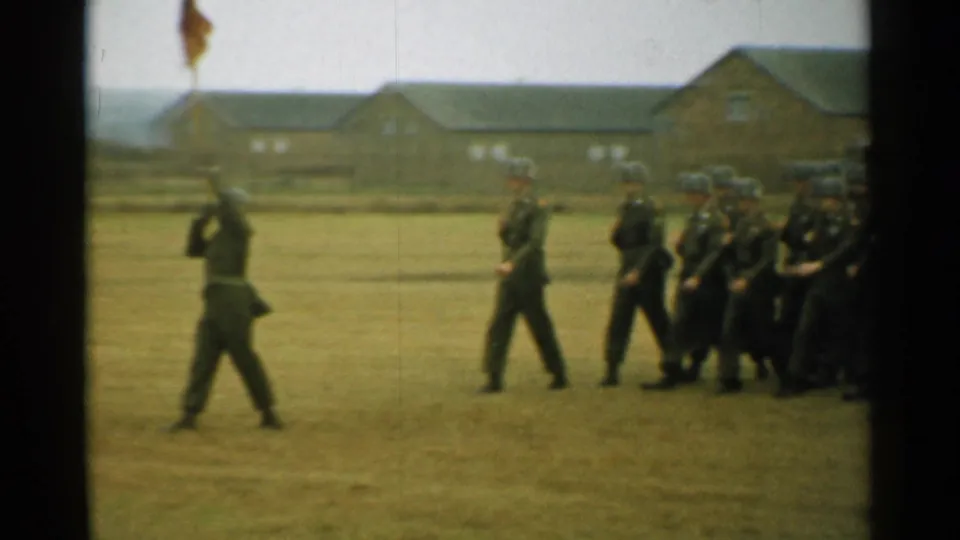 A flag bearer leads helmeted soldiers across a grassy base field in 1952 New Hampshire archival home-movie footage.