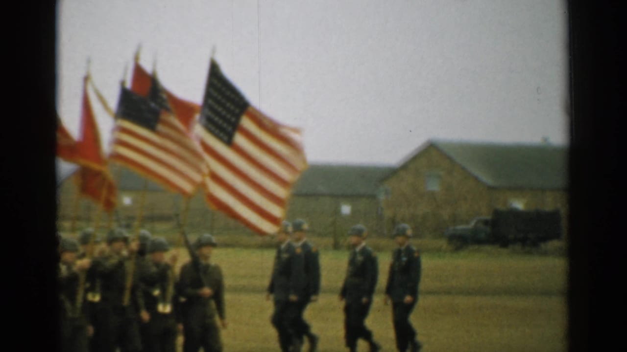 Color guard detail carries American flags and red banners during a 1952 New Hampshire military-base march.
