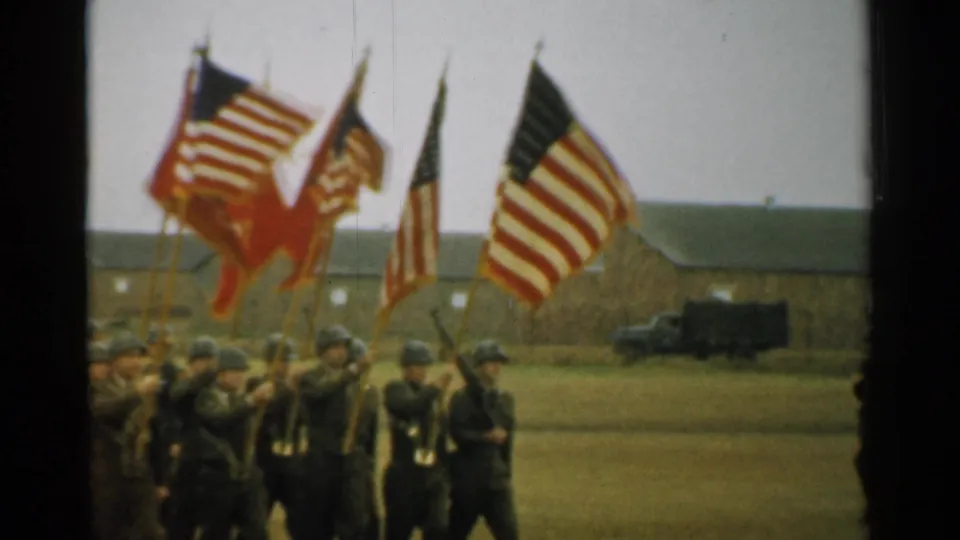 Color guard soldiers carry American flags and banners across a grassy New Hampshire base field in 1952.
