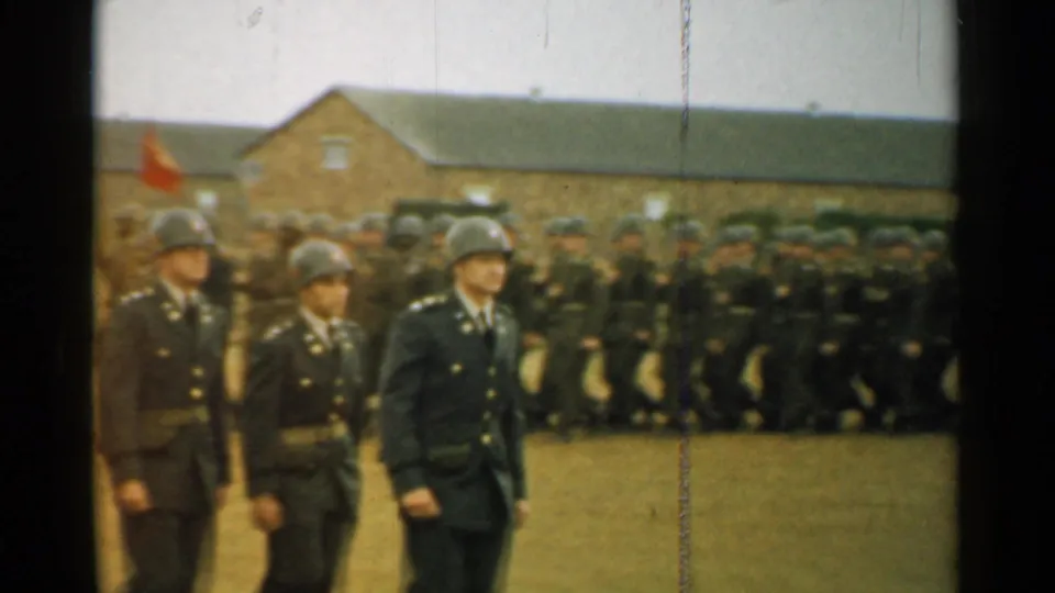 Soldiers in dark military uniforms and helmets march past a dense formation near brick barracks in 1952 New Hampshire footage.