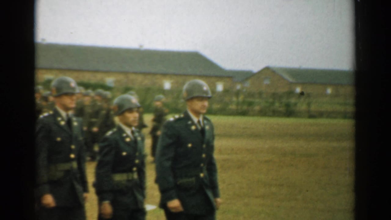 Soldiers in dark uniforms and metal helmets march across a grassy field.