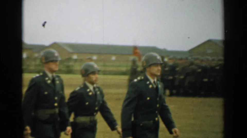 1952 New Hampshire military-base view of helmeted soldiers marching in dress uniforms, with troops and barracks visible in the background.