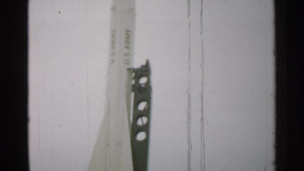 1952 New Hampshire frame with the pointed upper section of a U.S. Army-marked rocket beside a perforated metal support tower.