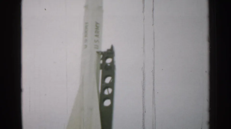 1952 New Hampshire frame with the pointed upper section of a U.S. Army-marked rocket beside a perforated metal support tower.