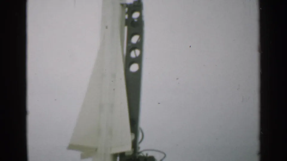1952 New Hampshire 8mm frame showing the lower rocket body, flared base or fins, and dark launch support during a vertical pan.