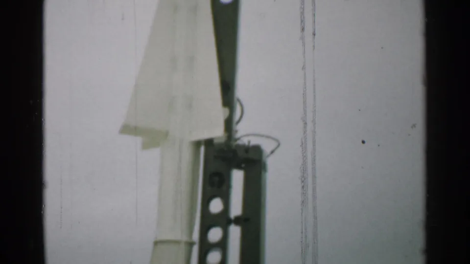 1952 New Hampshire frame showing the lower part of the white rocket next to a dark metal launch structure with circular cutouts and hardware.
