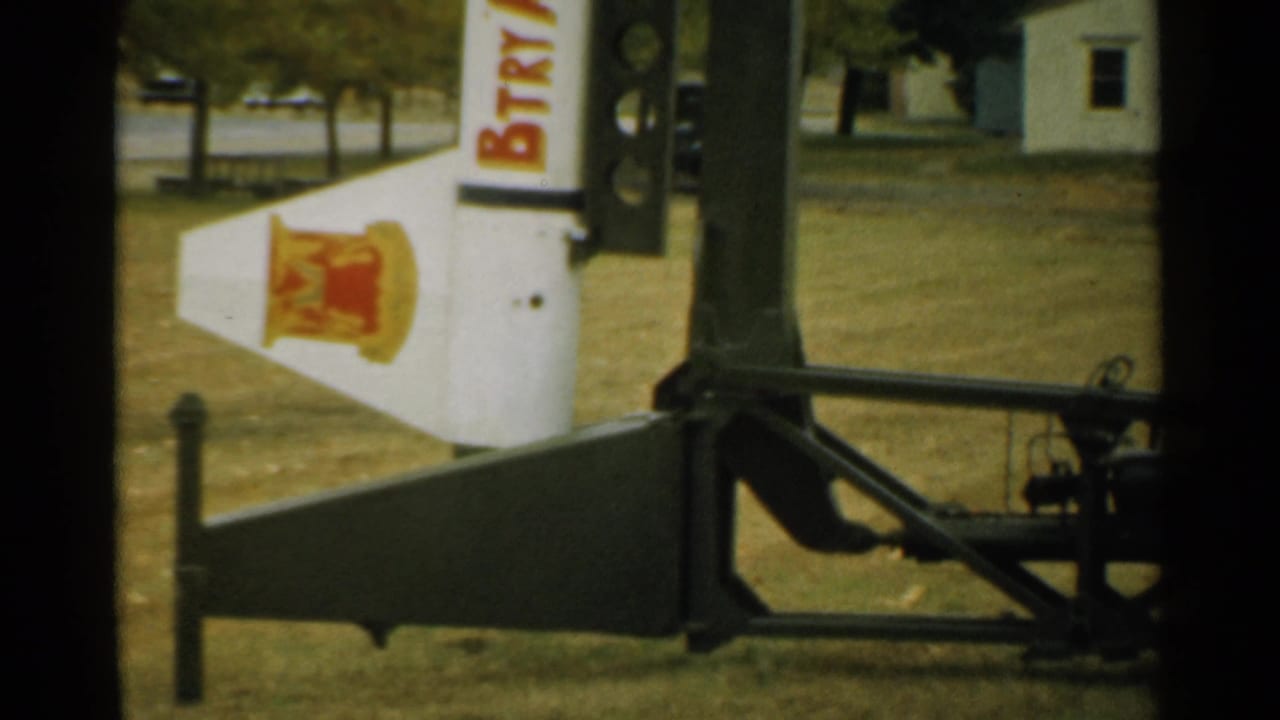 Partial white sign with red lettering beside a structure on a grassy outdoor area.