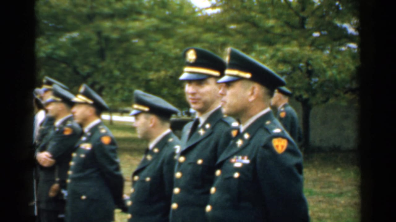 Uniformed military officers stand outdoors in a line, facing left.