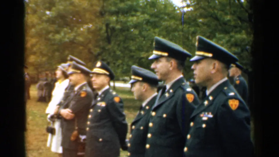 1952 New Hampshire 8mm frame showing uniformed officers and a person in white standing outdoors during a formal observation.