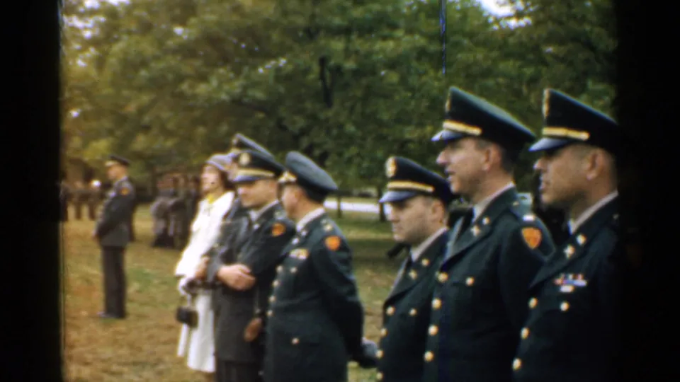 1952 New Hampshire frame of officers in dress uniforms and nearby observers watching an outdoor activity off camera.