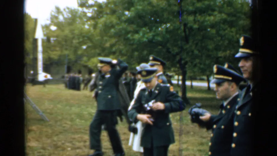 1952 New Hampshire frame showing officers in dress uniforms, some holding cameras, near a public outdoor ceremony.