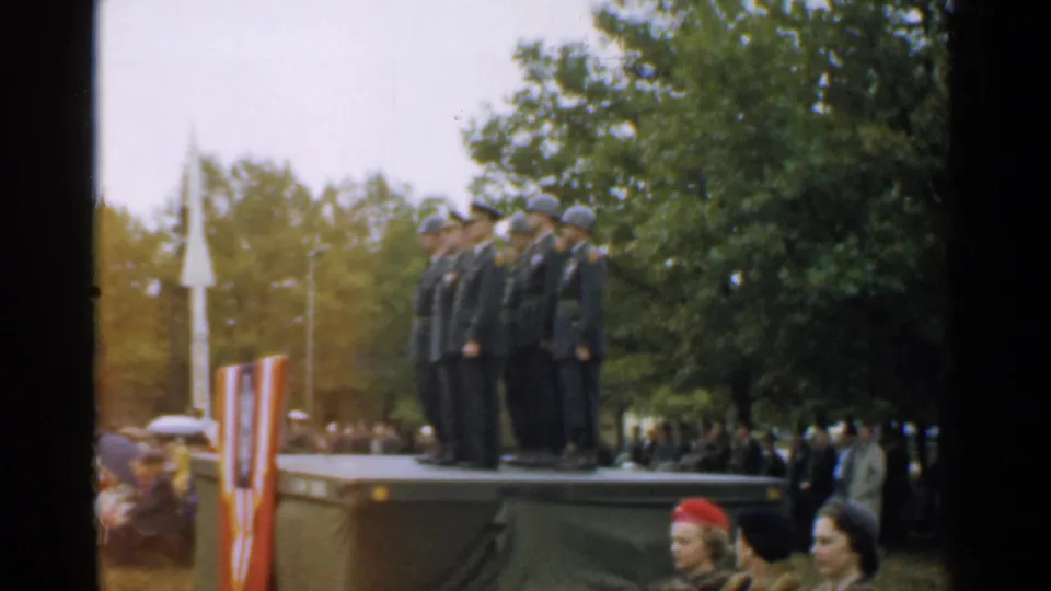 The 1952 home movie shows uniformed men saluting from a raised stage with civilians gathered around the outdoor ceremony.
