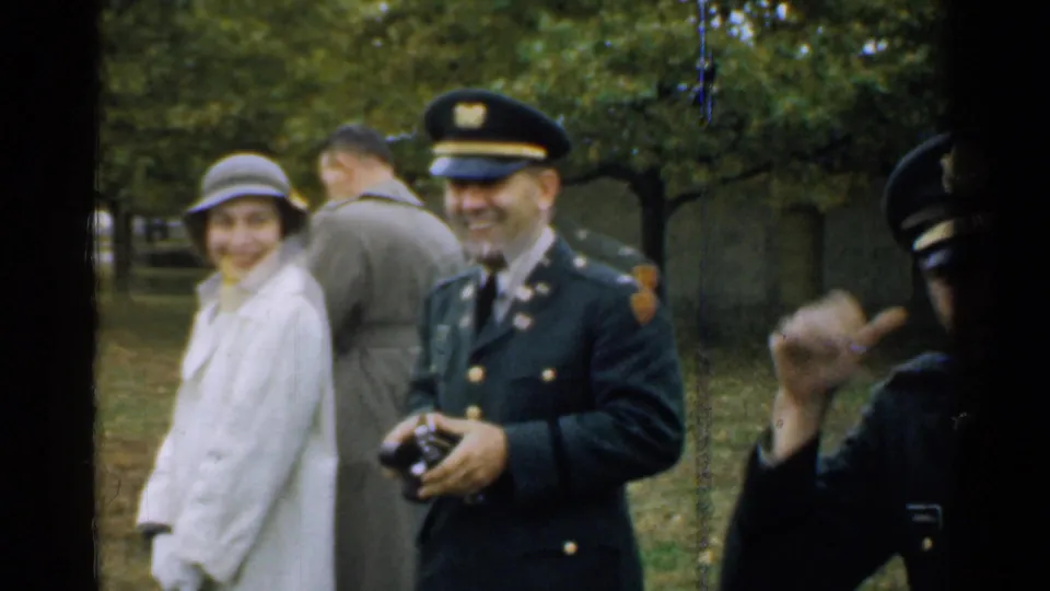 1952 New Hampshire home-movie still with a uniformed officer smiling, a woman in a hat, and another uniformed figure at frame edge.
