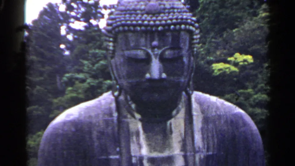 1953 Japan 8mm frame showing the face and shoulders of a large outdoor Buddha statue against dense green trees.