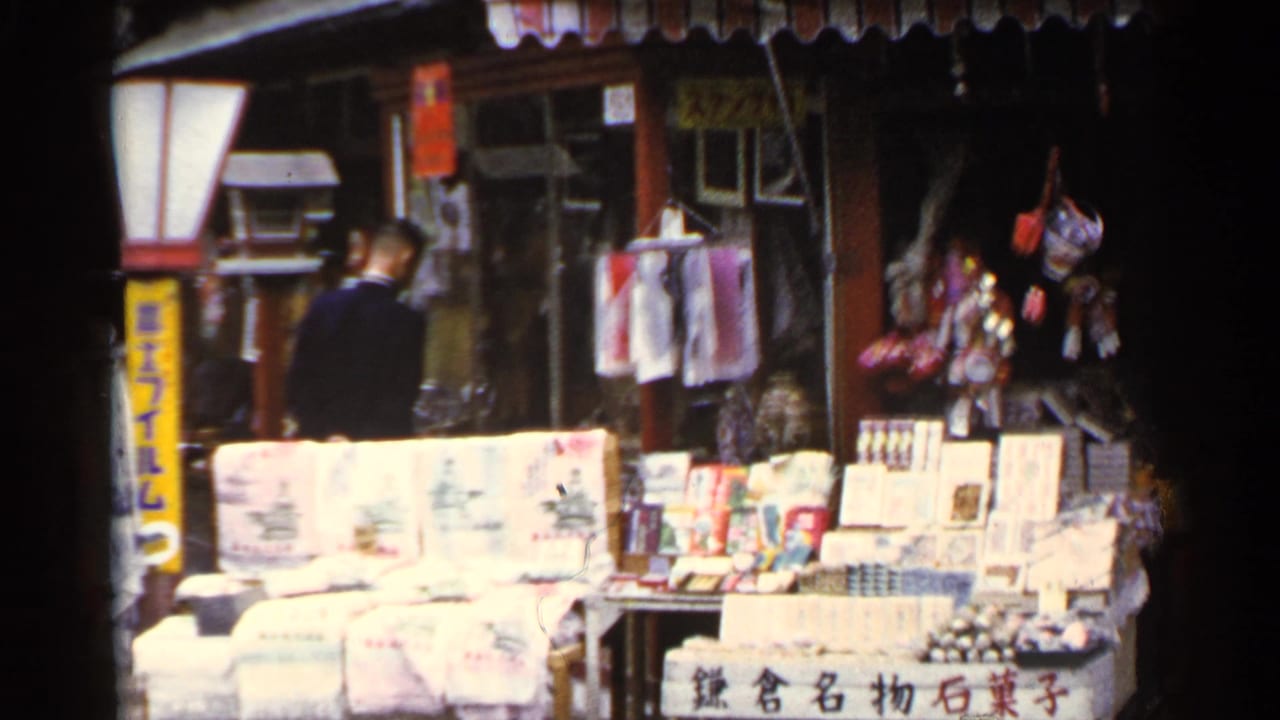 Person in dark clothing stands beside a Japanese market stall with stacked goods and signage.