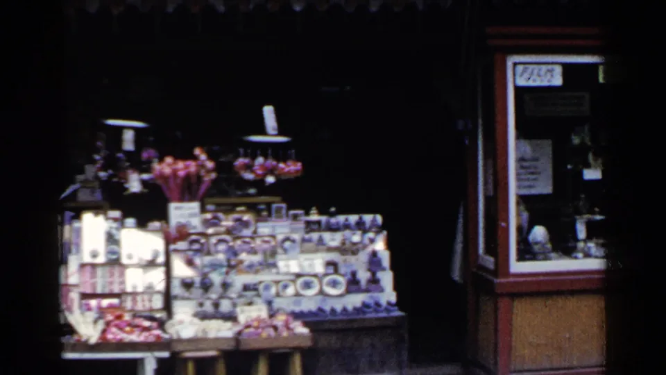A closer 8mm view shows the souvenir table crowded with boxed items, figurines, and small goods under a dark storefront.