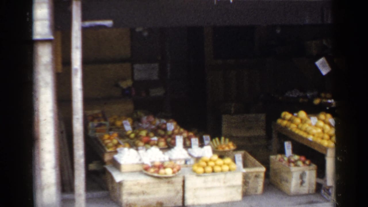 Fruit and produce displayed in wooden crates outside a shaded shop.