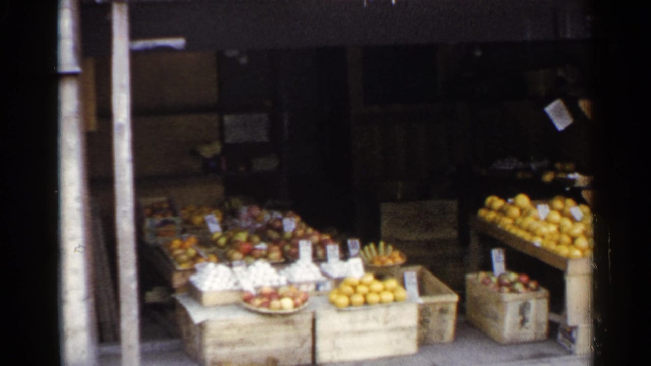 1953 Japan home-movie frame showing wooden crates of citrus and other fruit arranged at an open-front produce stall.