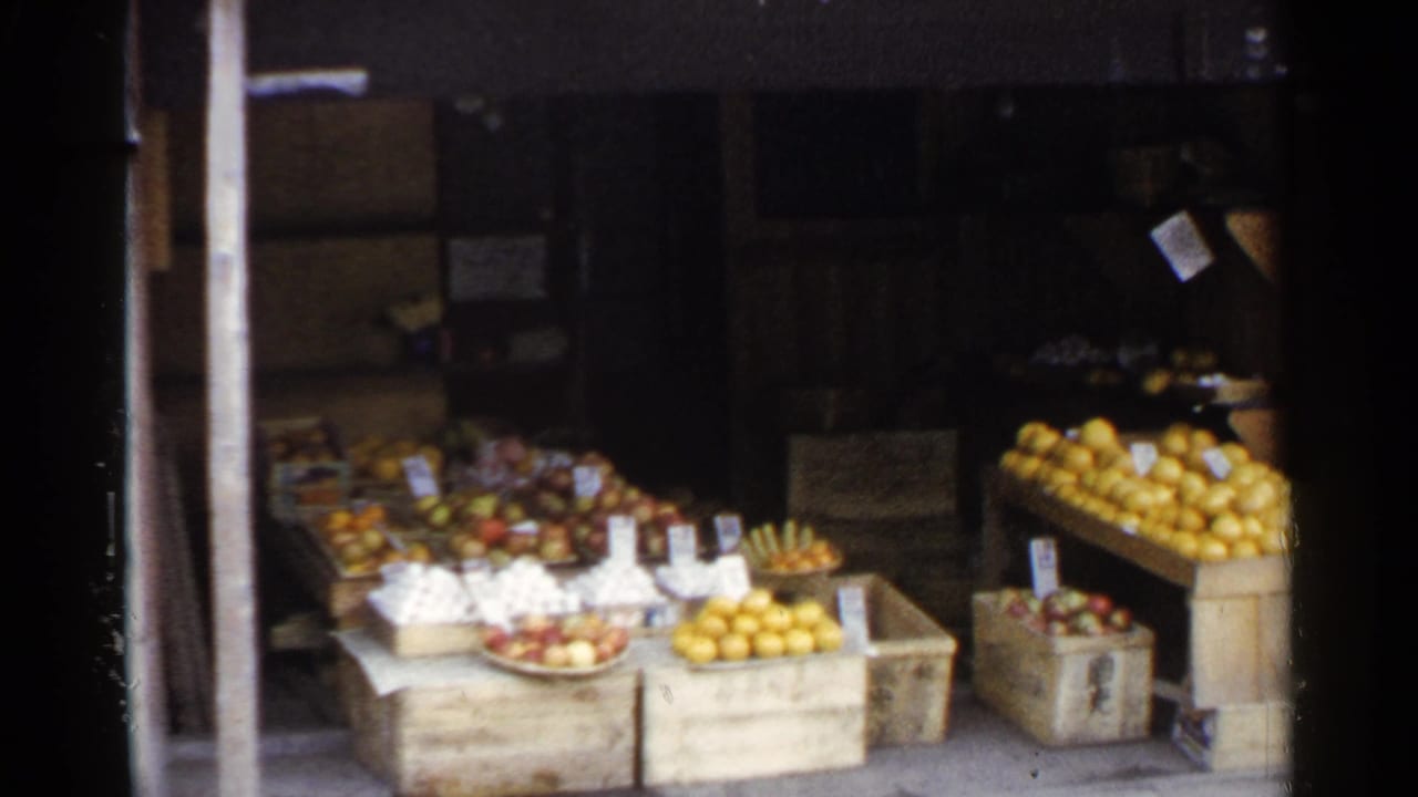 1953 Japan frame with citrus, mixed fruit, wooden boxes, and handwritten signs at a street produce stand.