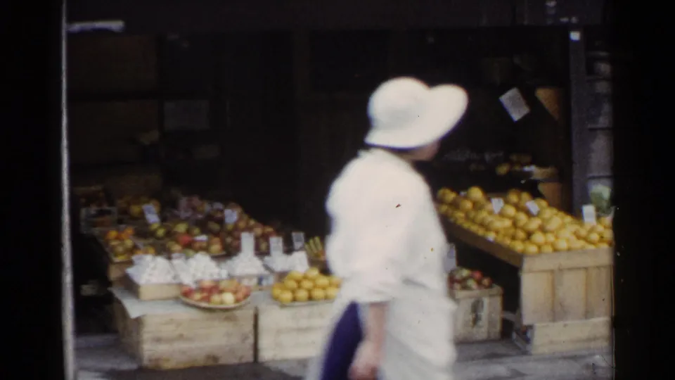 1953 Japan market frame showing a woman passing in front of wooden crates filled with citrus and other produce.