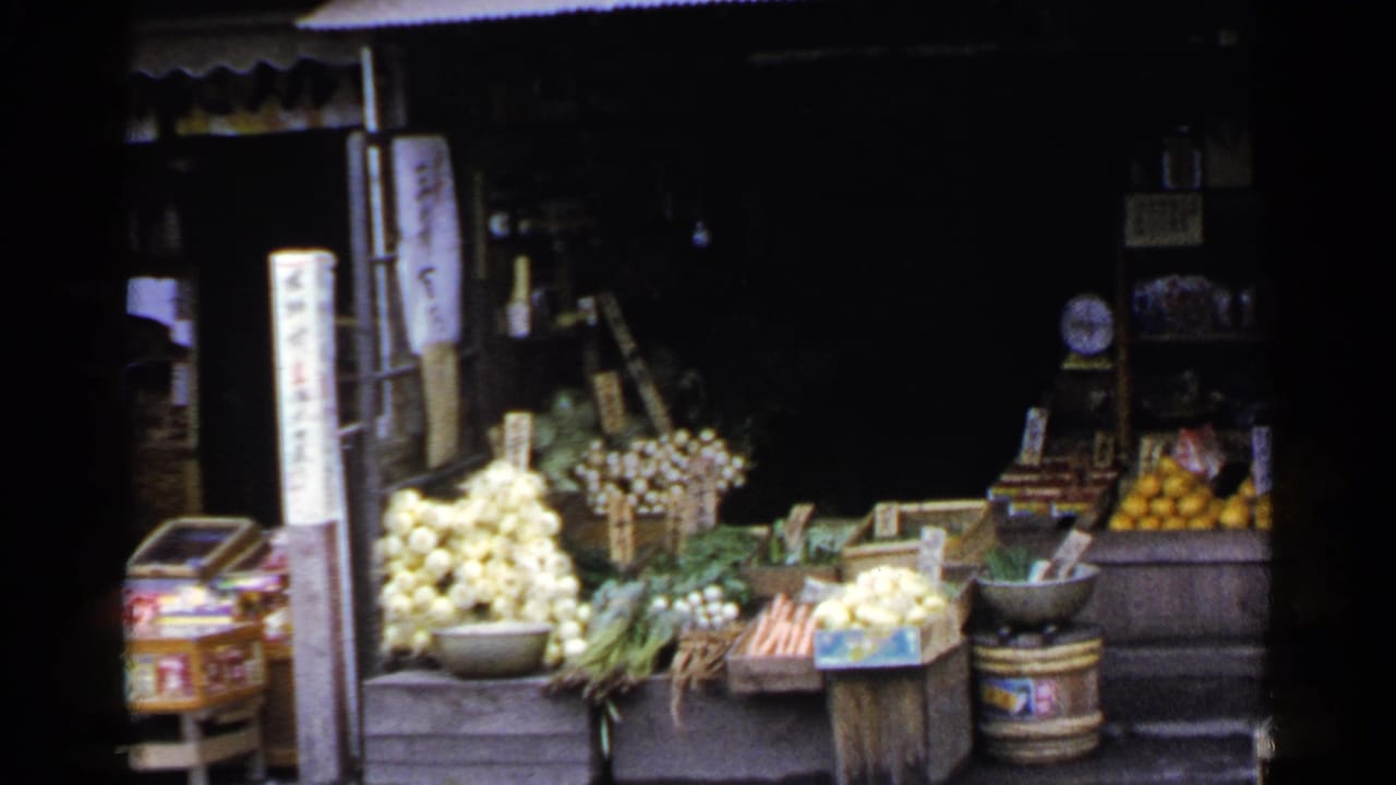 Street-facing produce stand with onions, carrots, greens, oranges, crates, and Japanese signs.