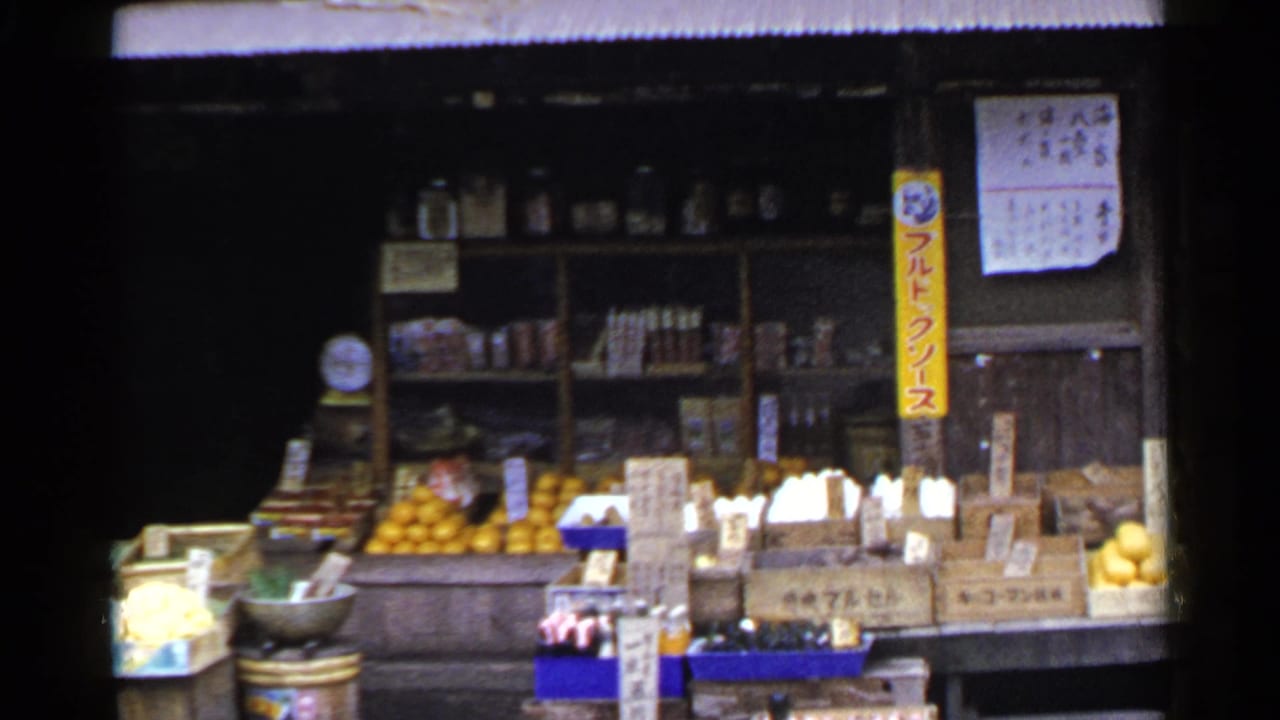 Produce stall with oranges, boxed foods, vertical Japanese sign, and shop shelves in the background.