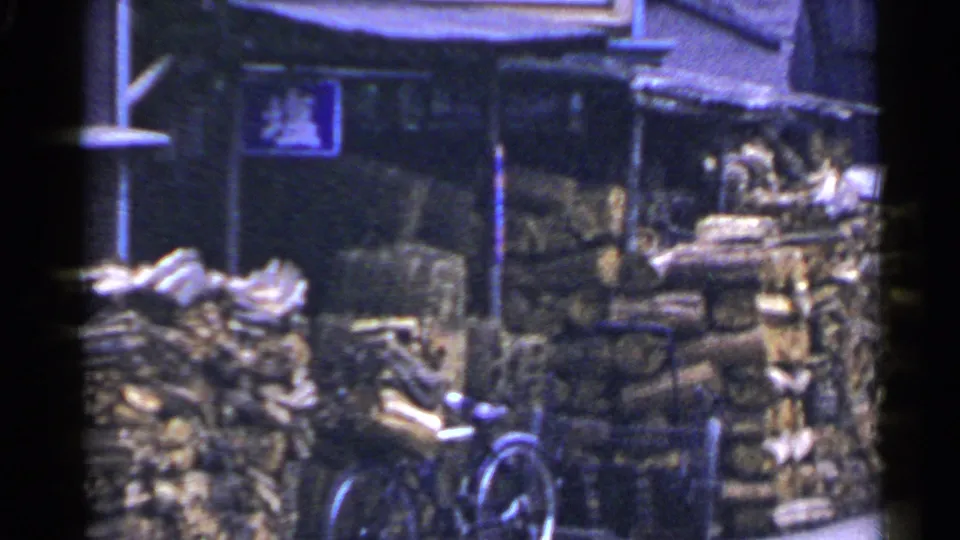 A later frame shifts to stacked chopped wood by a bicycle near the market area, with dark shopfront details and signage in the background.