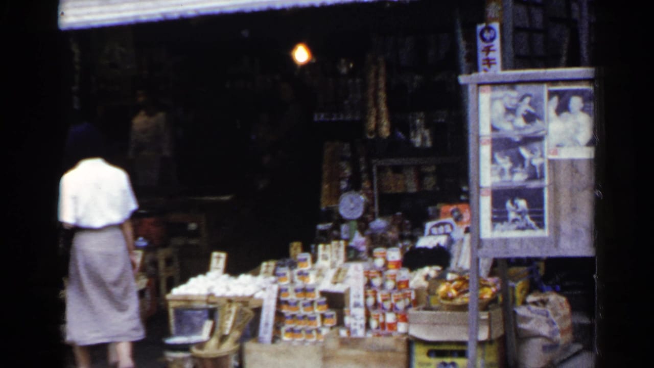 Woman in a white blouse approaches a Japanese market stall with stacked goods under an awning.