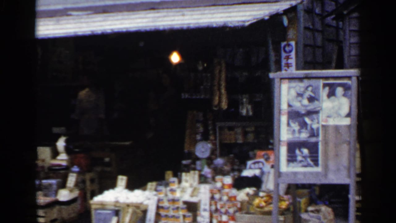 Food market storefront with stacked goods, photo board, awning, and a dim interior.