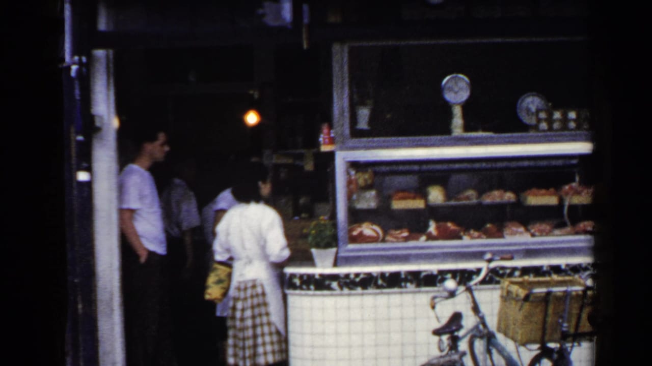 1953 Japan street-side deli scene with an apron-wearing worker, waiting customers, displayed food, and a bicycle at the counter.