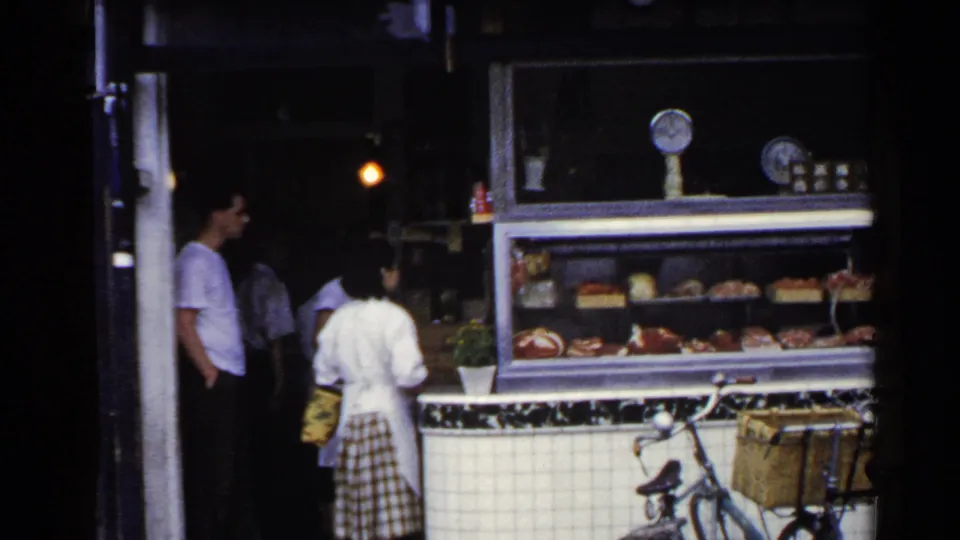 1953 Japan street-side deli scene with an apron-wearing worker, waiting customers, displayed food, and a bicycle at the counter.