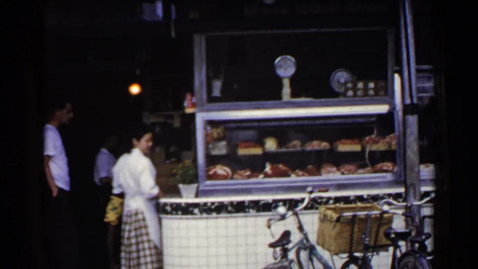 1953 Japan frame showing a quiet shopfront exchange around a deli counter, with food display, staff, customers, and bicycle basket visible.