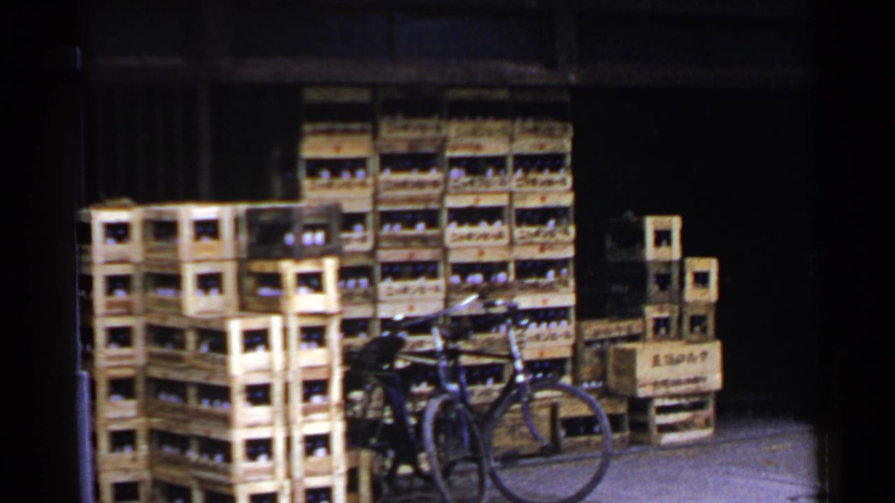 1953 Japan 8mm frame showing stacked wooden bottle crates at a dim warehouse opening with a bicycle in front.