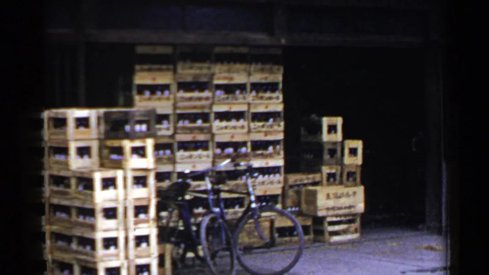1953 Japan 8mm view of wooden bottle crates and a bicycle at a dim warehouse or shop entrance.