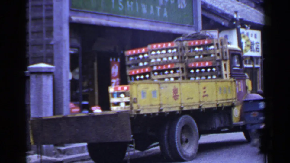 1953 Japan street frame showing a yellow delivery truck carrying bottle crates in front of a building with signage.