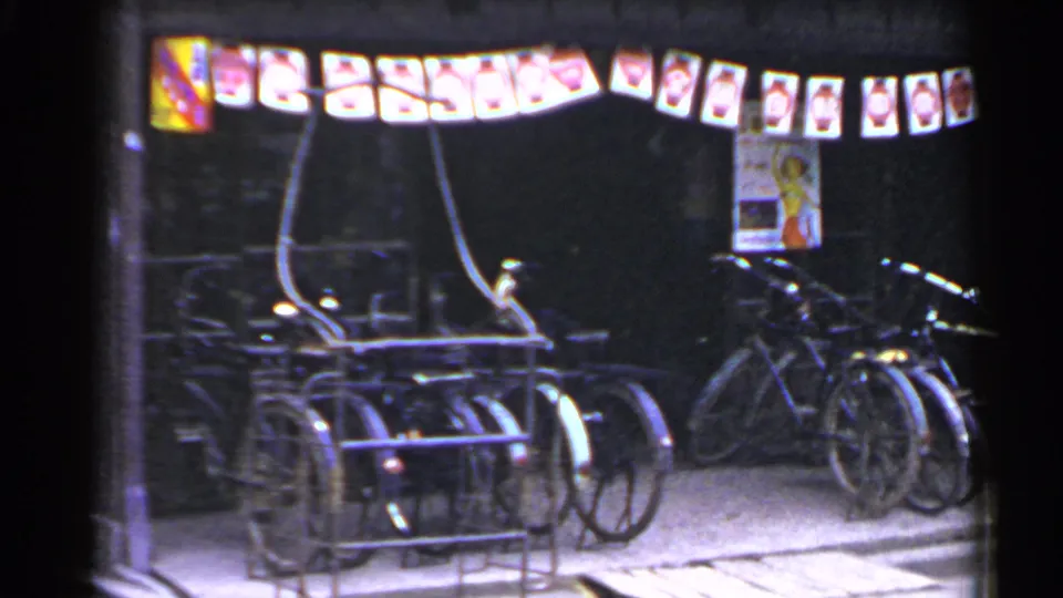 1953 Japan street view with parked bicycles, a rack, lanterns, posters, and a dark storefront at night.