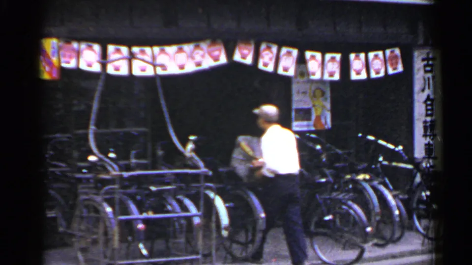 1953 Japan frame showing a man in a white shirt handling a bicycle near a rack under lanterns at night.