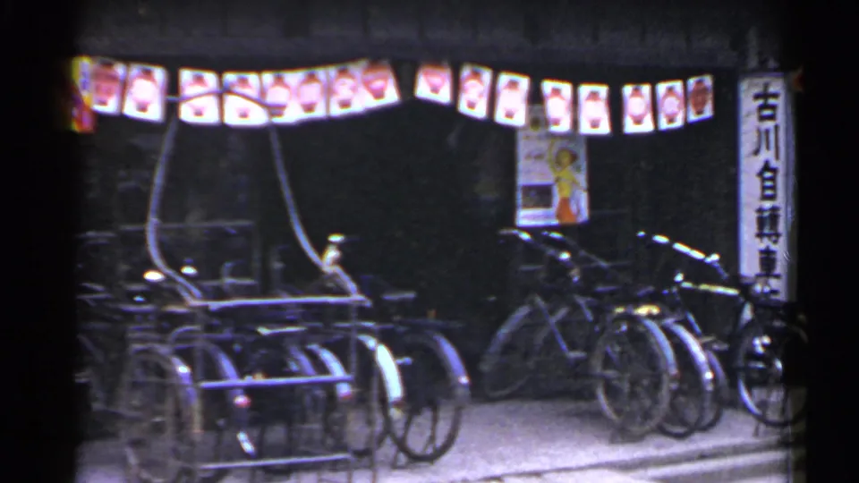 1953 Japan nighttime street frame with parked bicycles, a rack, lanterns, posters, and vertical signage.