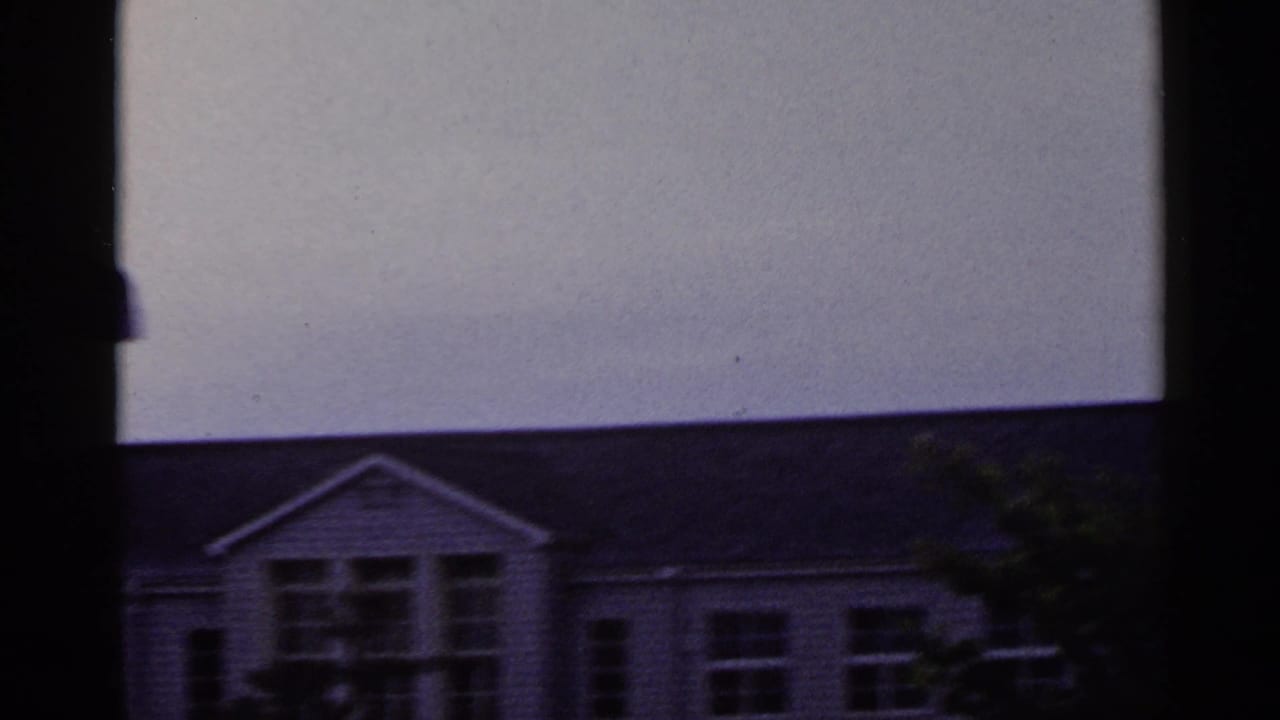 1953 Japan 8mm frame centered on a gabled building section, windows, roofline, and pale overcast sky.