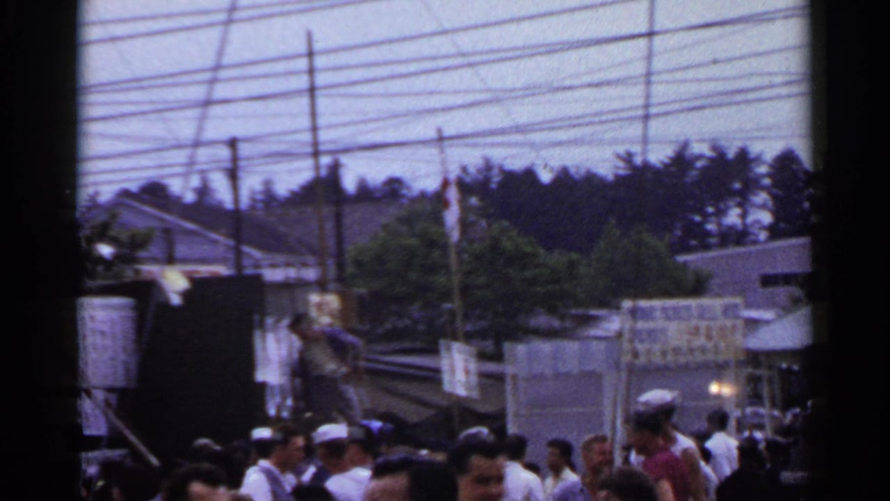 Street fair crowd with sailors, booth structures, trees, and overhead power lines.