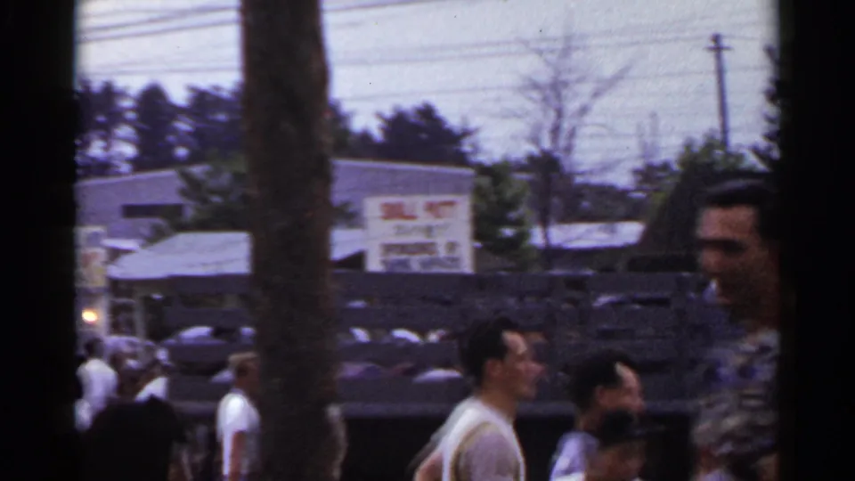 Street-fair crowd in Japan, 1953, with foreground faces, a tree trunk, painted signage, buildings, and overhead wires.